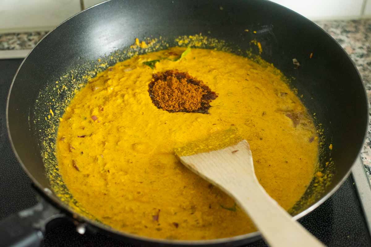powdered jaggery added to a curry in a wok