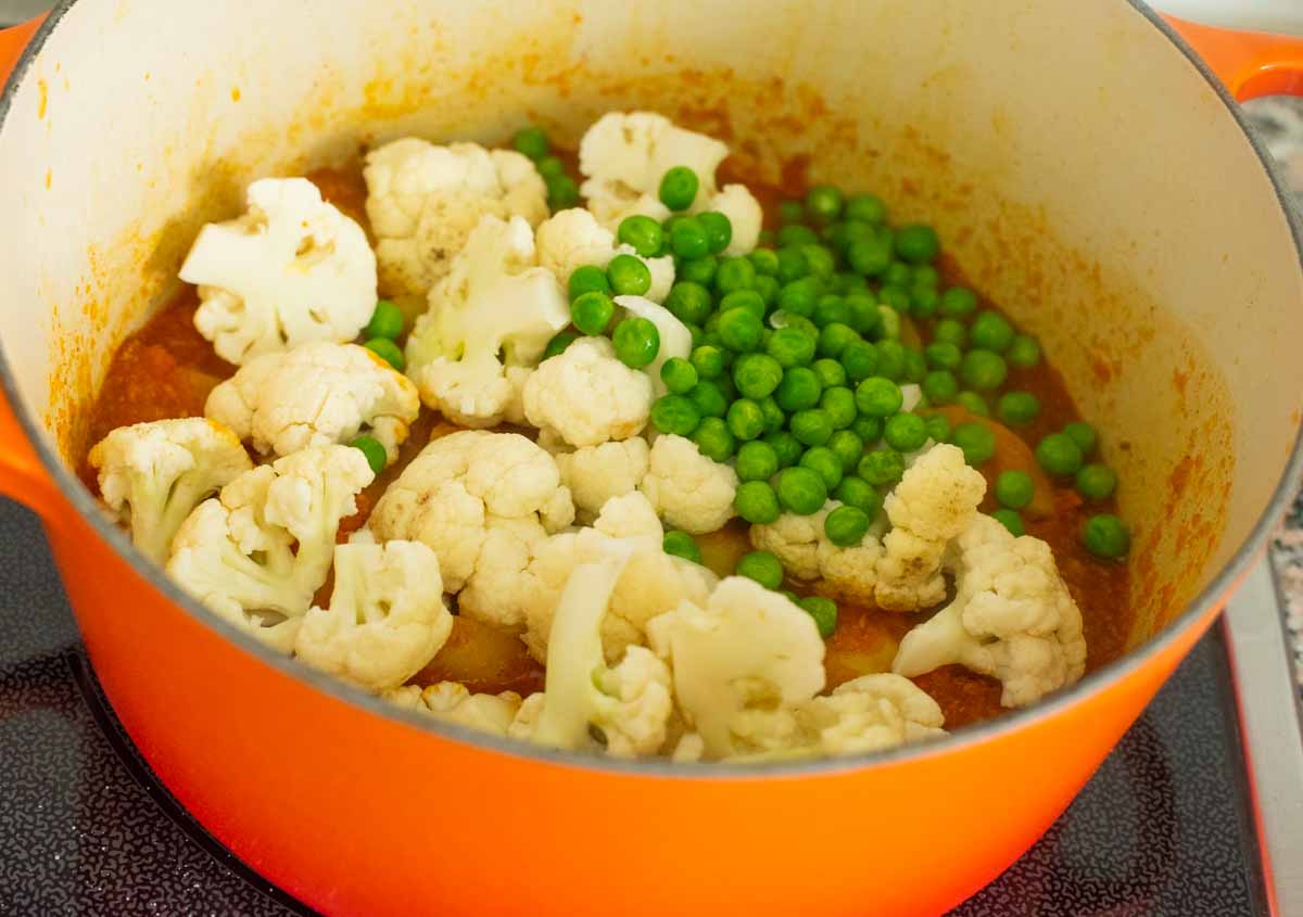 cauliflower and peas added to a curry in a pot on stovetop