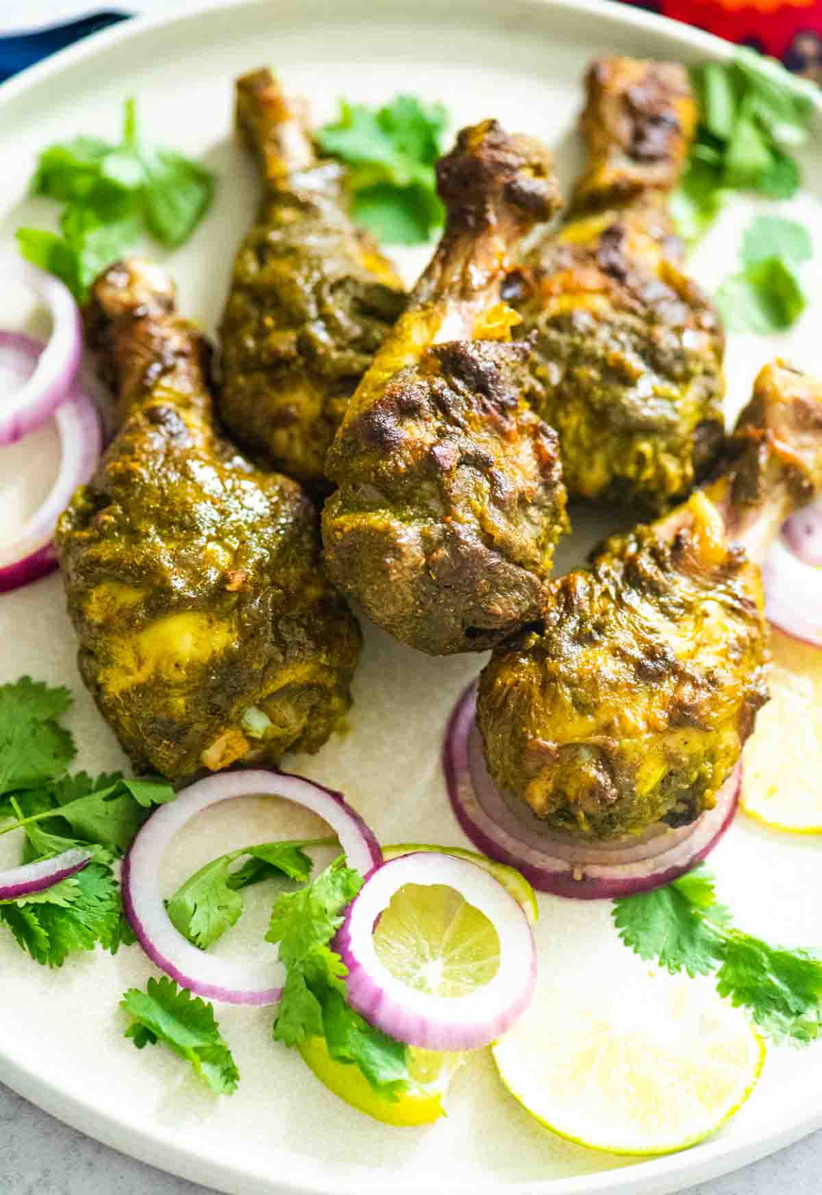 Green Chicken Drumsticks on a plate with lemon cilantro and red onions