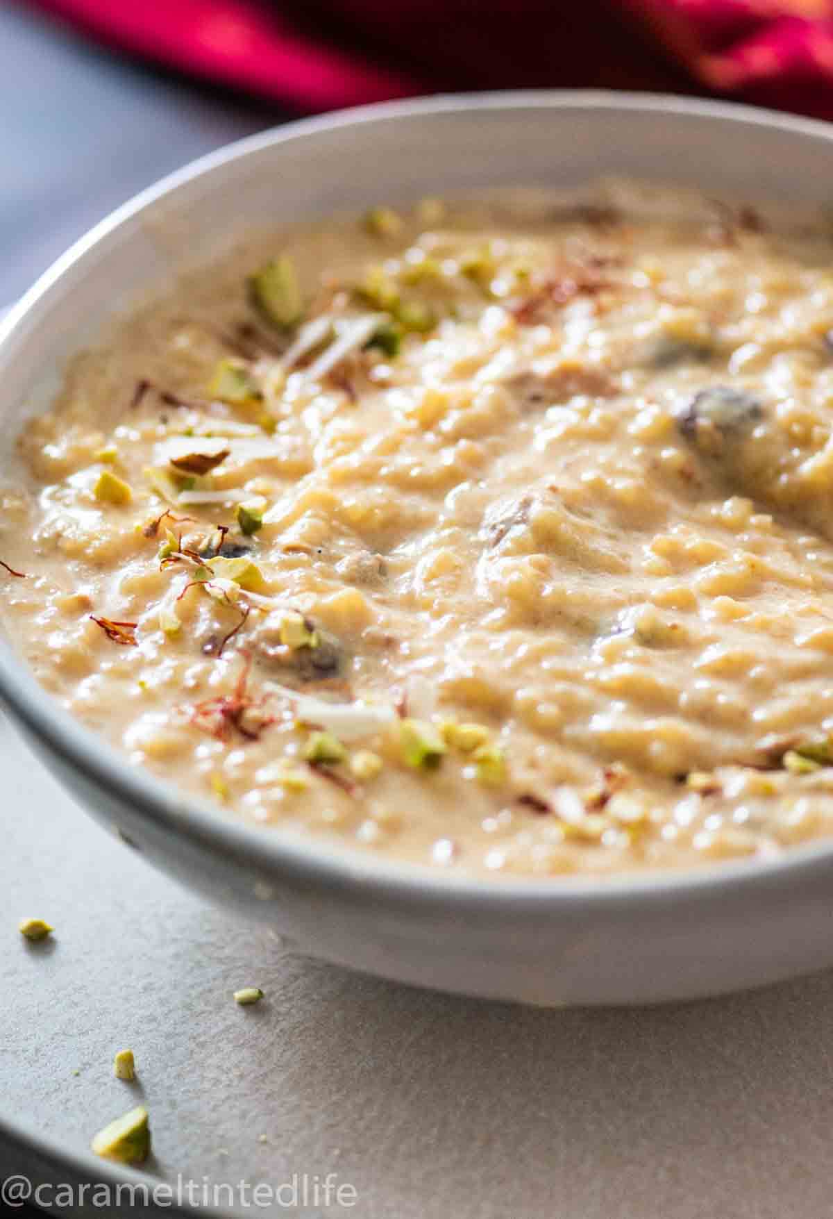 close up of a bowl of rice kheer with saffron and nut garnish