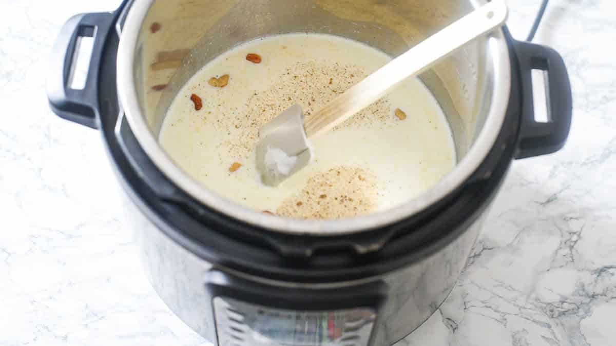 Instant Pot with milk, cardamom powder, spatula and other ingredients