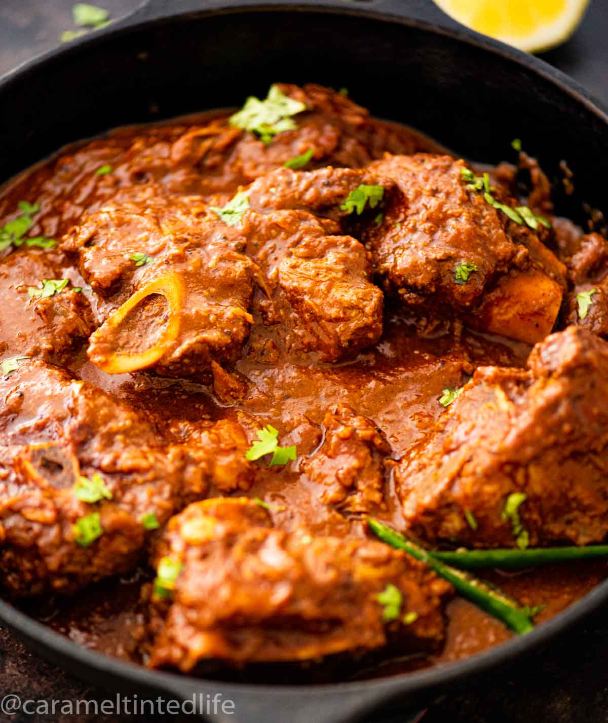 lamb curry in a cast iron pot with slit green chili garnish