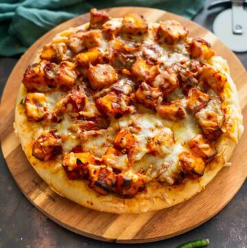 round pizza with paneer and tomato sauc etopping on a wooden board