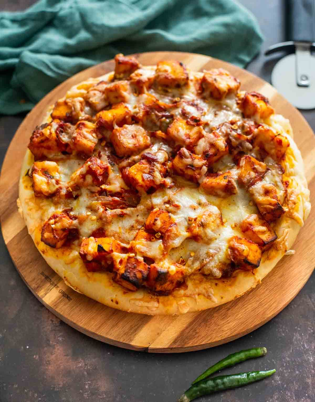 round pizza with paneer and tomato sauc etopping on a wooden board
