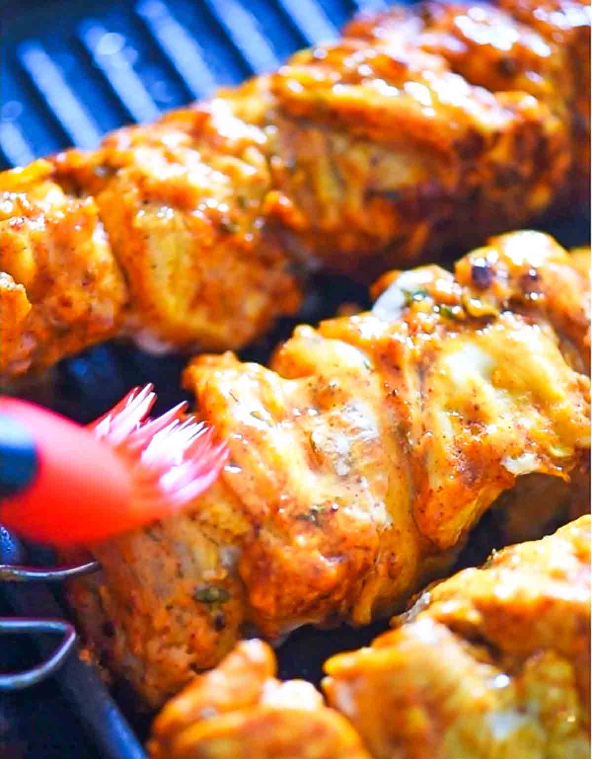 brushing oil on chicken skewers being grilled
