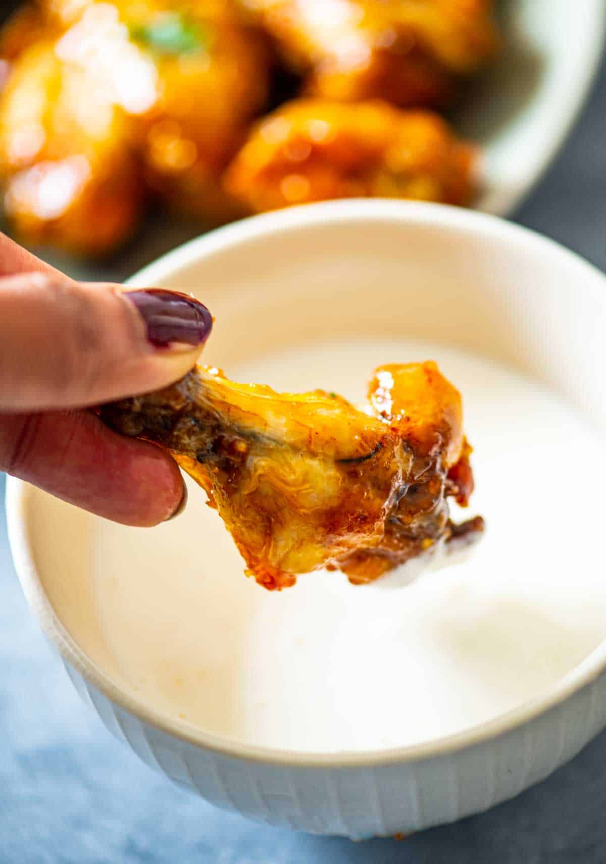 fingers holding a chicken wings over a dip bowl