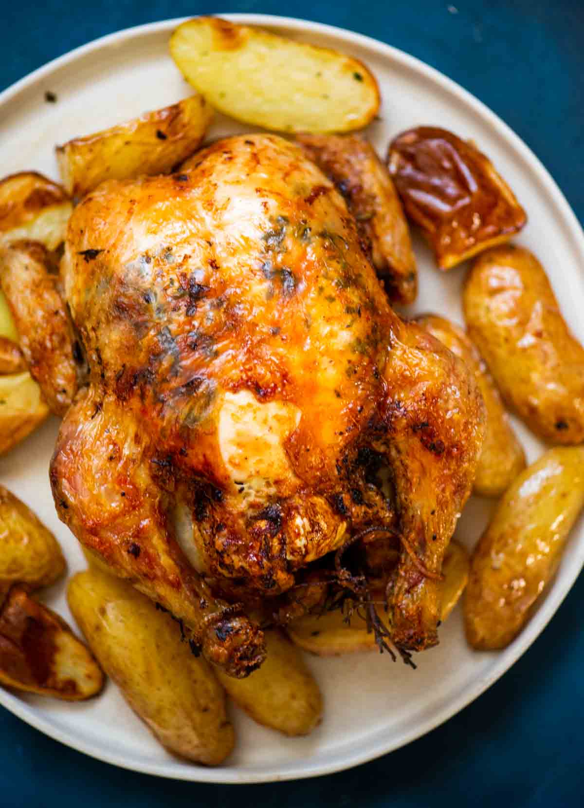 whole roasted chicken on a plate with roasted potatoes