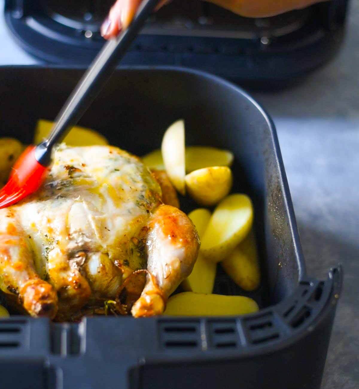 chicken being based with oil in air fryer basket