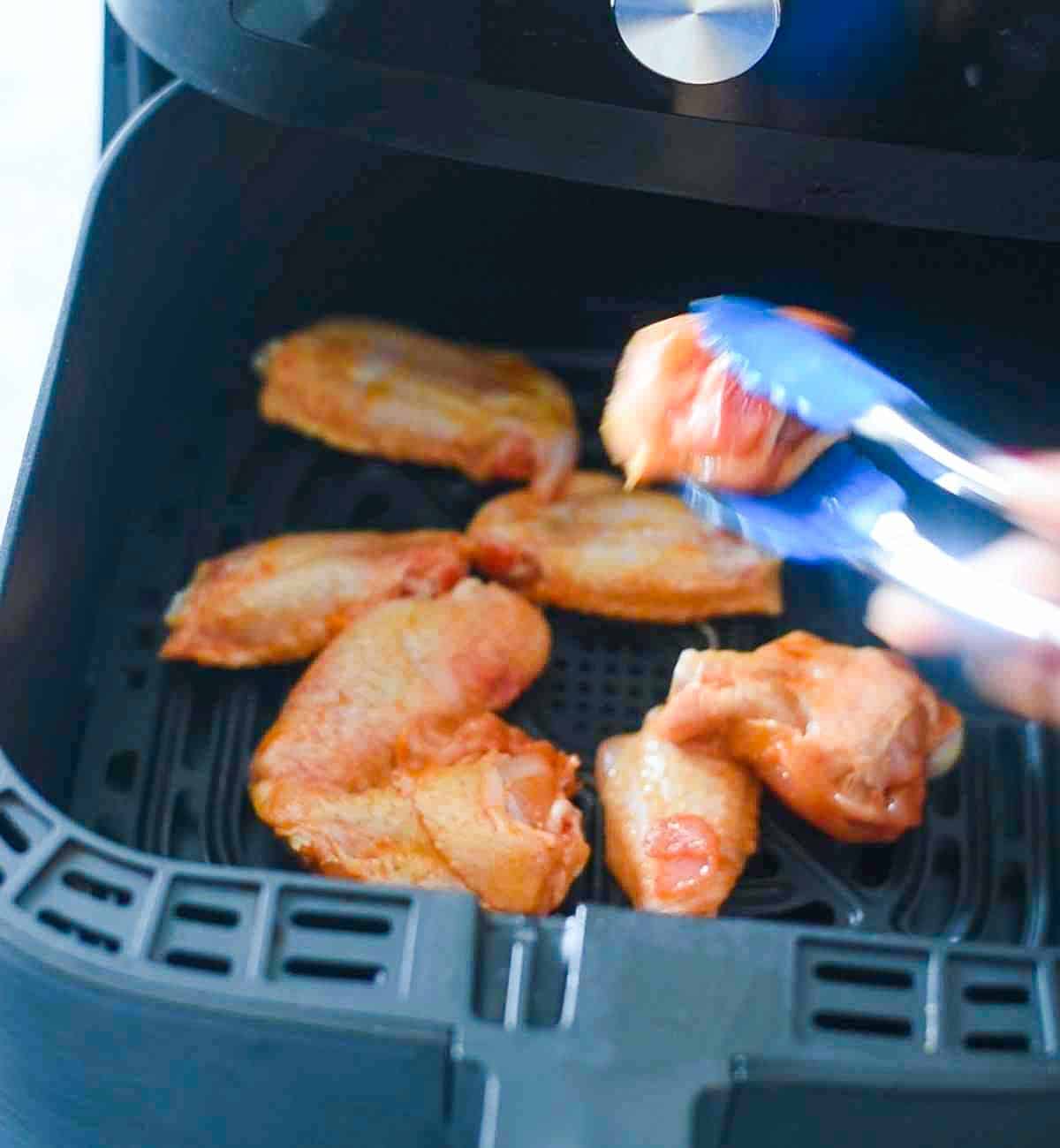 tongs holding chicken wings in an air fryer basket