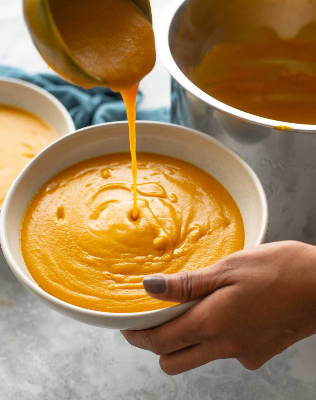 hand holding a bowl of pumpkin soup