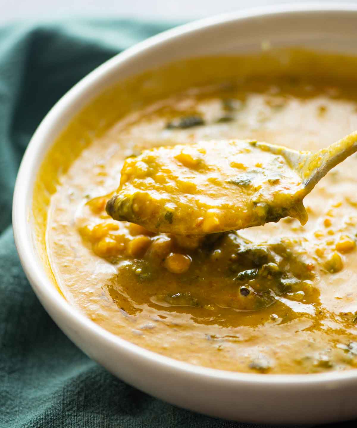 spoon holding dal palak over a bowl of dal