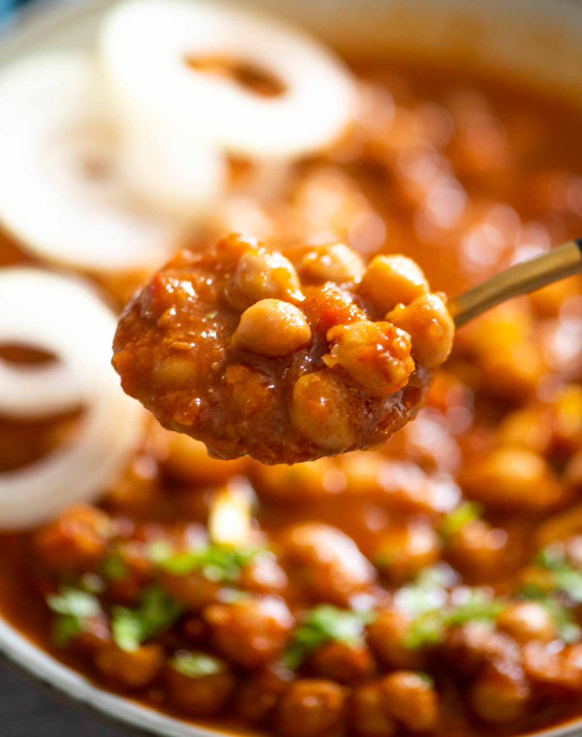spoon holding chole or chickpea curry over a bowl