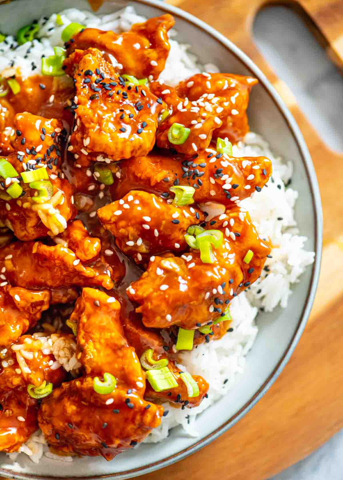 side view of orange chicken on a bed of rice in a bowl