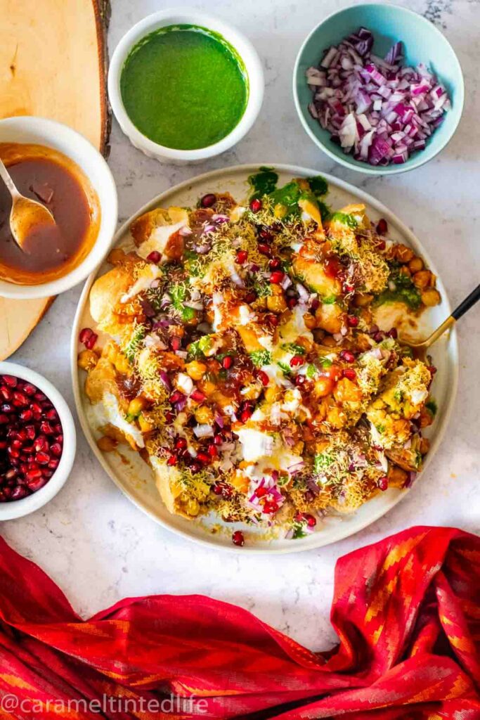 top view of samosa chaat with a red cloth and garnishes around it