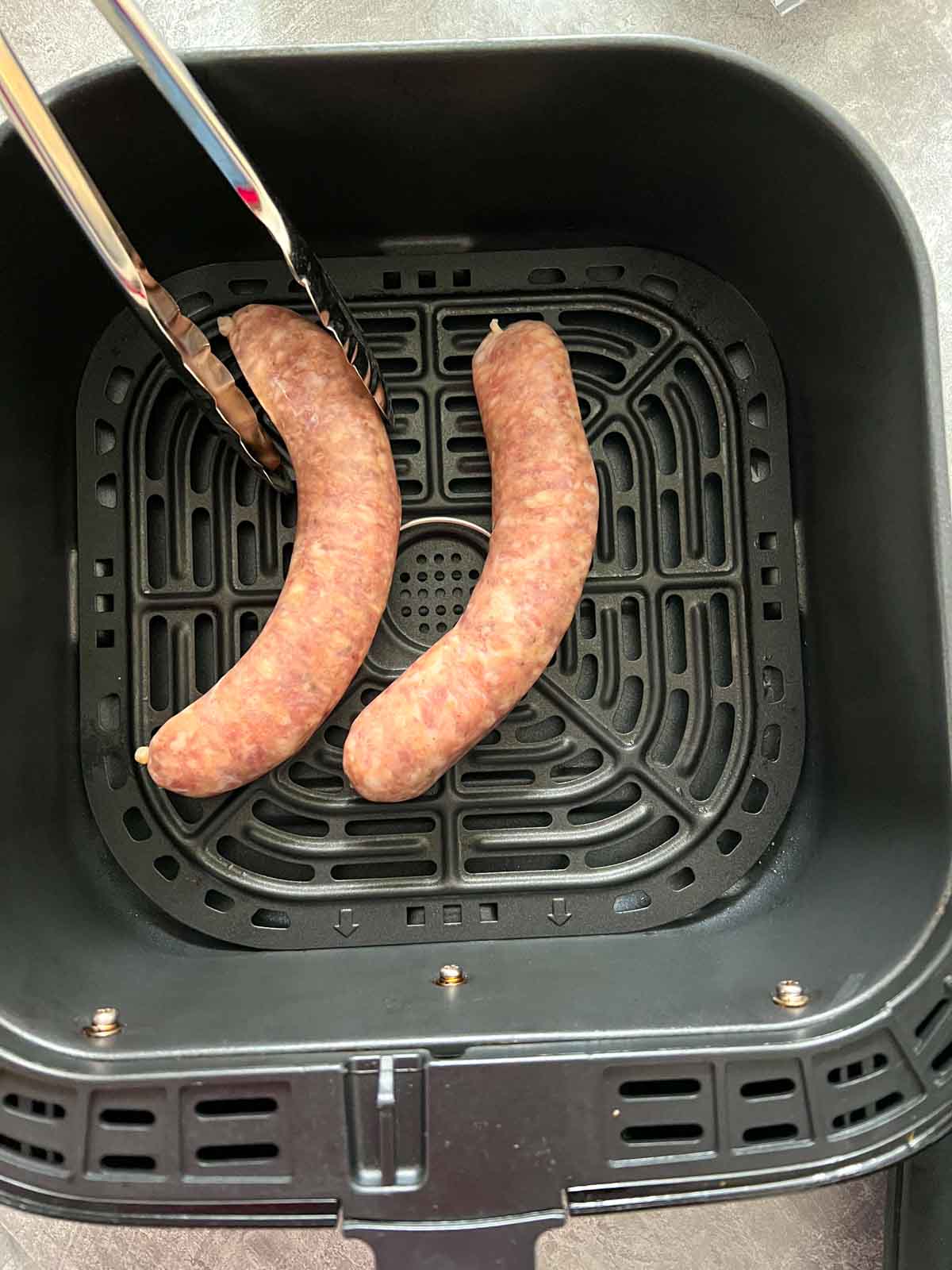 raw sausages placed in air fryer basket