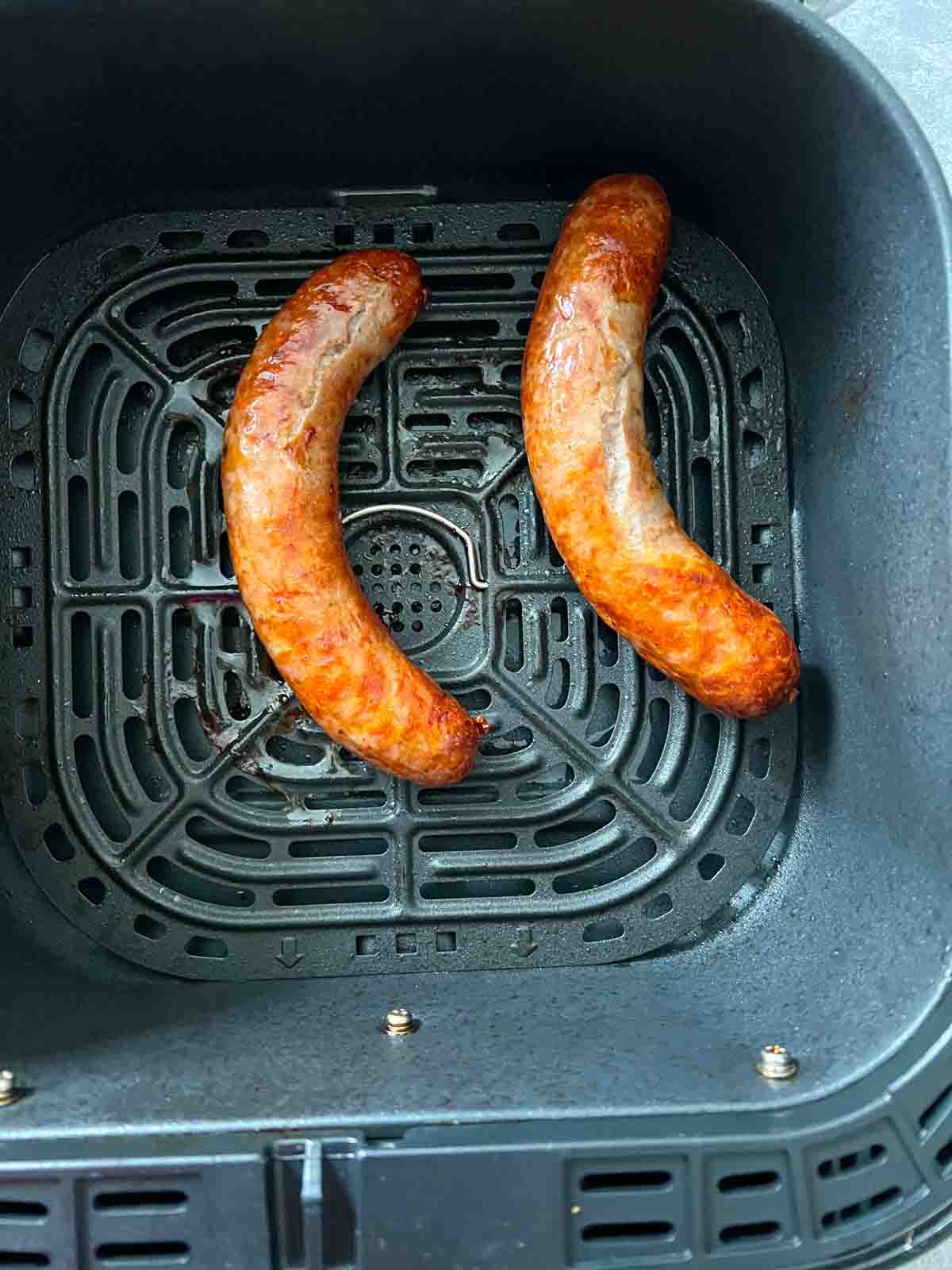 two cooked sausages in air fryer basket