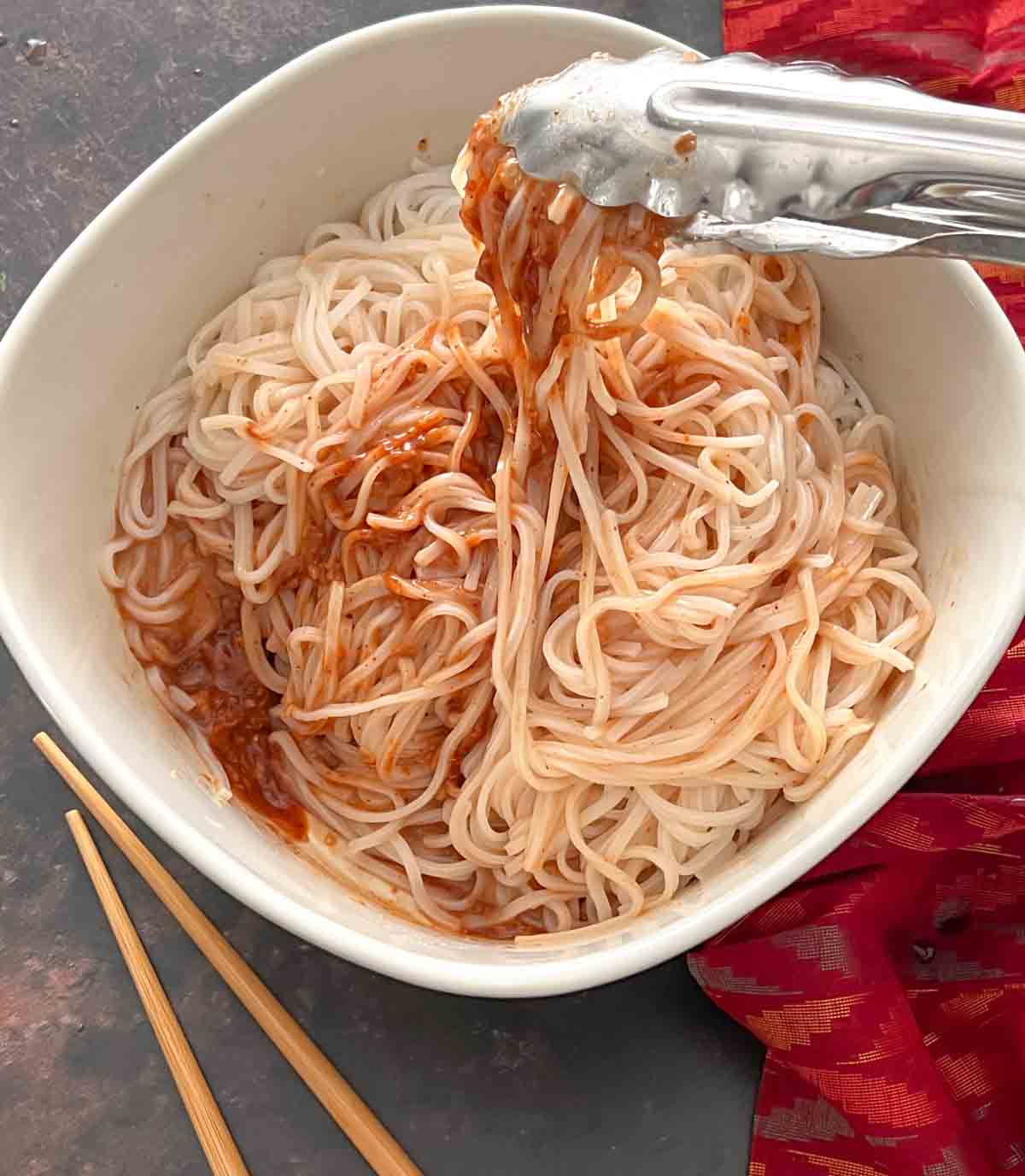 tongs mixing rice noodles in sauce